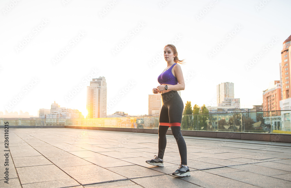 Street portrait of a fitness girl in sportswear that does sports against the background of the sun and looks into the camera. Morning sports charge during sunrise. Street portrait of a fitness girl in sportswear that does sports against the background of the sun and looks into the camera. Morning sports charge during sunrise.