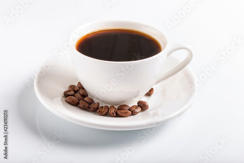 a cup of coffee with coffee beans on a plate, isolated on white.