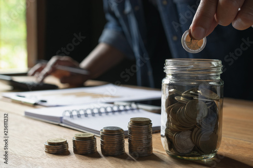 Business man putting coin in glass bottle saving bank and account for his money all in finance accounting concept.