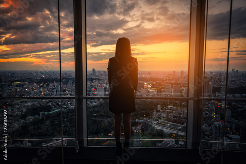 Rear view of Traveler woman looking Tokyo Skyline and view of skyscrapers on the observation deck at sunset in Japan. © nuttawutnuy