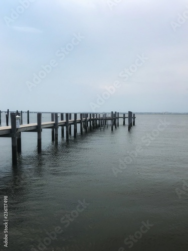 Long wood pier stretching out into the bay with blue sky and horizon.