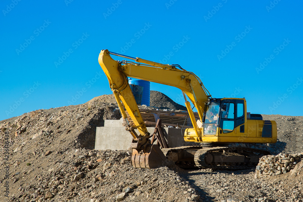 The excavator rakes in stones with his bucket. Excavator rakes rocky ground. Yellow excavator in work. The excavator rakes in stones with his bucket. Excavator rakes rocky ground. Yellow excavator in work.