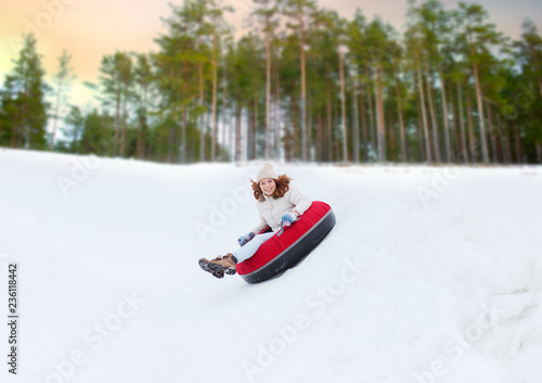 winter, leisure and entertainment concept - happy teenage girl sliding down hill on snow tube