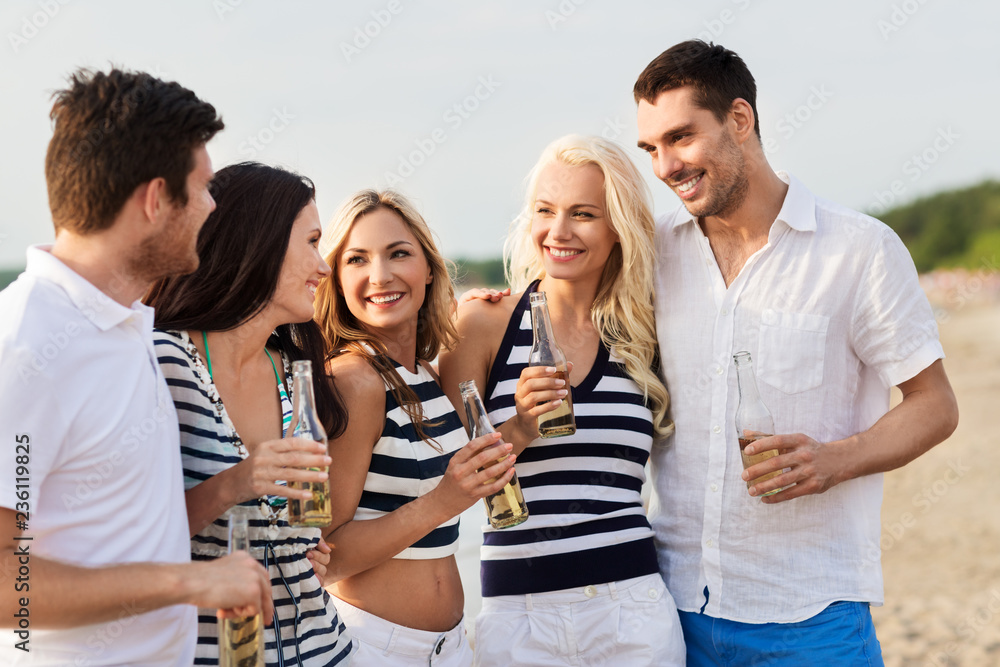 Obraz premium friendship, summer holidays and people concept - group of happy friends in striped clothes drinking non alcoholic beer on beach