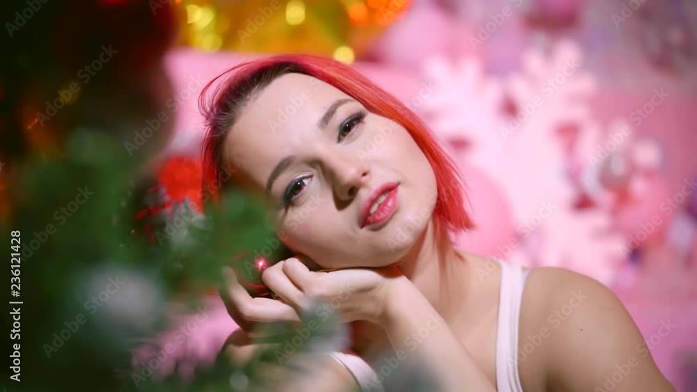 Cute young girl with red hair sitting at the Christmas tree and holding a glass ball Cute young girl with red hair sitting at the Christmas tree and holding a glass ball