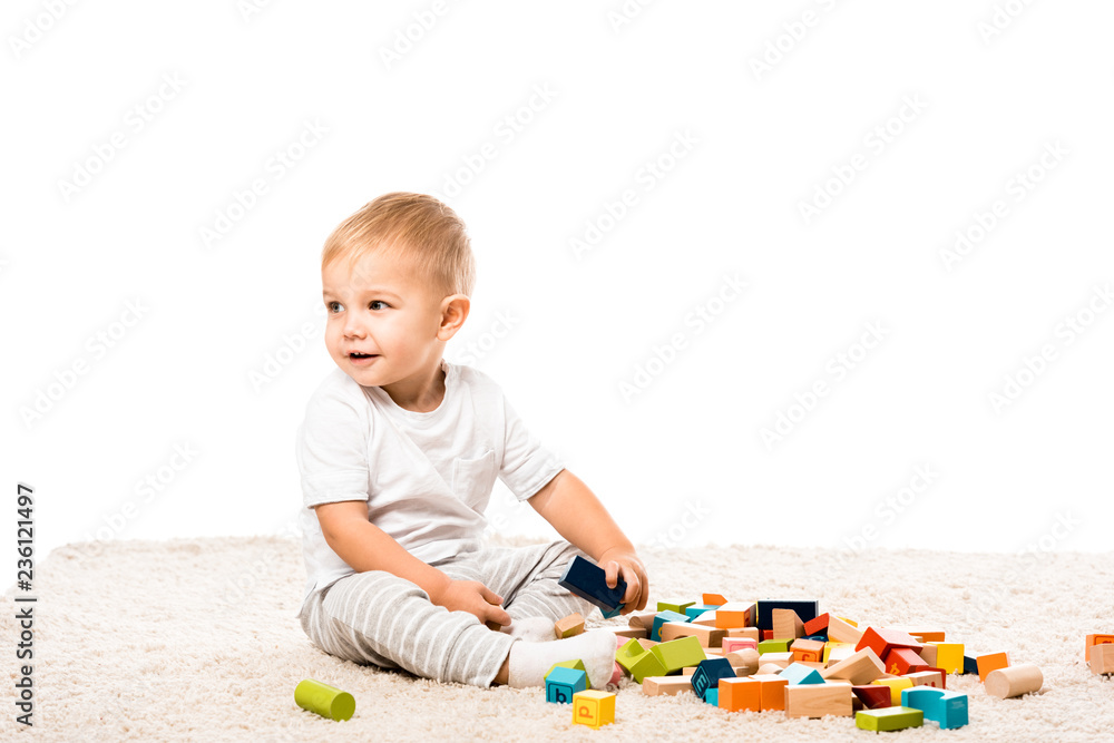 cute toddler boy smiling and playing with wooden blocks on carpet isolated on white cute toddler boy smiling and playing with wooden blocks on carpet isolated on white