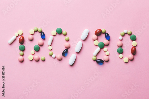 colorful tablets, capsules, pills shaped as blood pressure test results on pink background, creative medical diabetes treatment and blood pressure control concept, flat lay, top view
