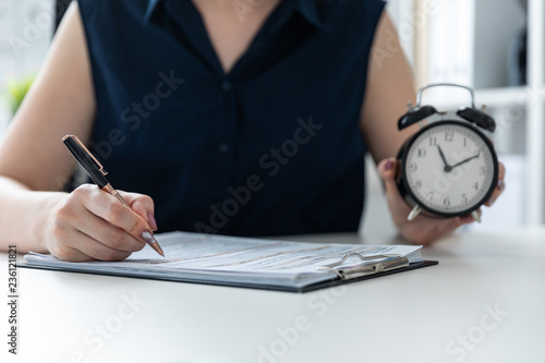 Women's hands holding a pen and an alarm clock. photo