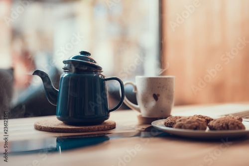 Laconic image of the ceramic cup standing near the teapot with steam over the table