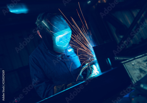  A vibrant action shot of a skilled working metal welder in action, welding metal. Photographed with a slow shutter speed and spark trails. Orange and teal.