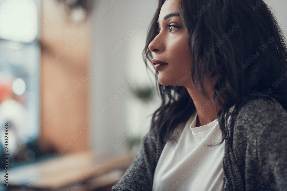 Naklejka premium Peaceful young dark haired woman sitting alone and thoughtfully looking into the distance