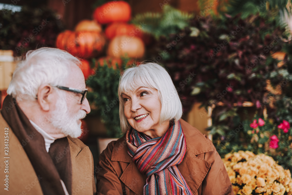 Portrait of smiling lady looking at husband with love and admiration. Flowers and pumpkins on blurred background Portrait of smiling lady looking at husband with love and admiration. Flowers and pumpkins on blurred background