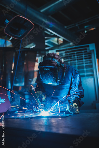 london, england, 02/02/2018 A vibrant action shot of a skilled working metal welder in action, welding metal. Photographed with a slow shutter speed and spark trails. Orange and teal.