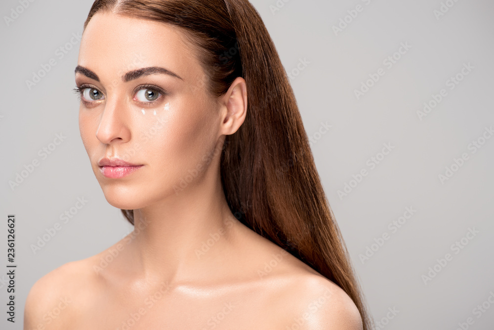 Fototapeta premium attractive nude girl with eye cream on face, isolated on grey