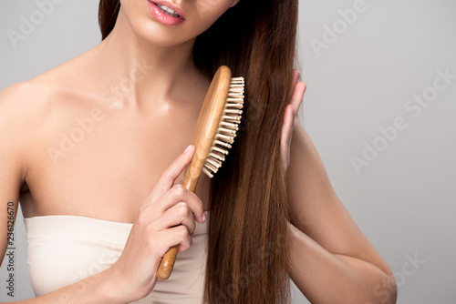 cropped view of woman combing hair with wooden hairbrush, isolated on grey