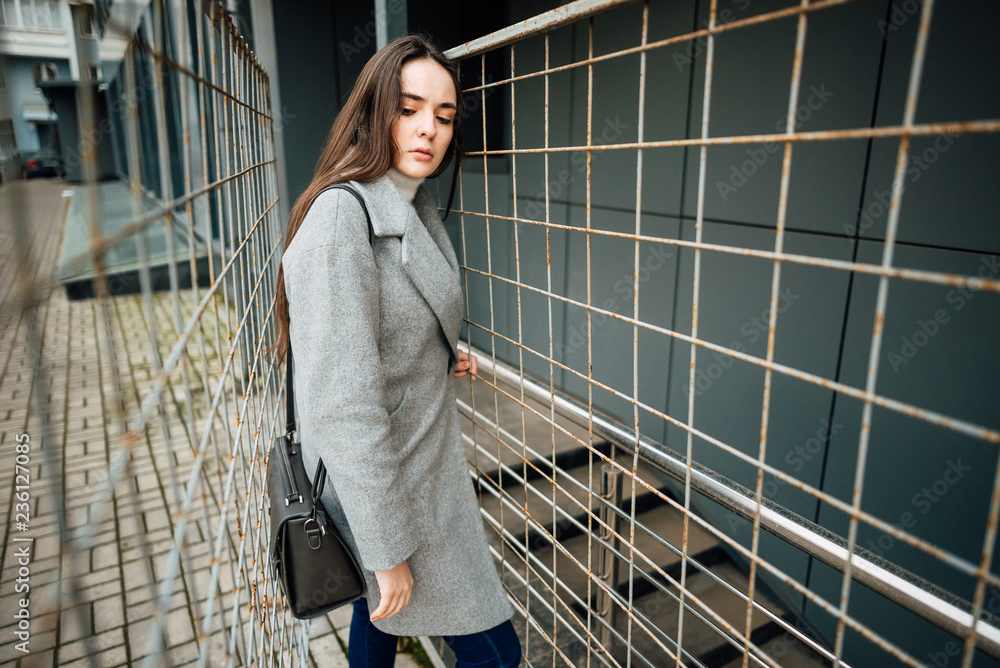 Fototapeta premium Beautiful young girl in a gray coat behind a fence outdoors