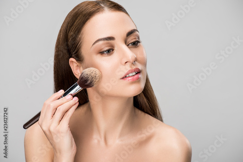 beautiful girl applying face powder with cosmetic brush, isolated on grey