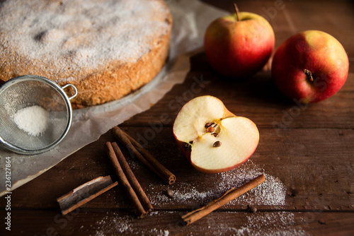 Homemade pie with apples and cinnamon sticks on wooden background.