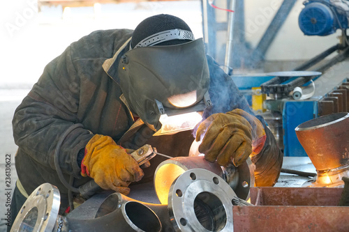 The professional welder works with manual-arc welding. Welds the pipe with the transition DN150. Butt weld.
