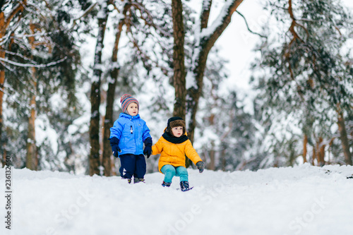 Two children going move down hill against snow-covered forest. Funny children's winter games