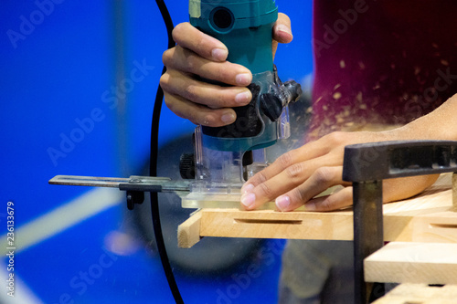 Carpenter working with electric planer on wooden plank in workshop