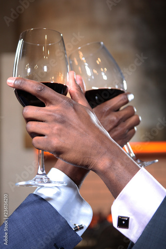 Two African-American hands with glasses of red wine in focus. Jacket and cufflinks, hands up. The concept of business meetings.