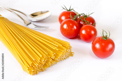 Spaghetti lie on a white background, along with cherry tomatoes, a spoon and a fork
