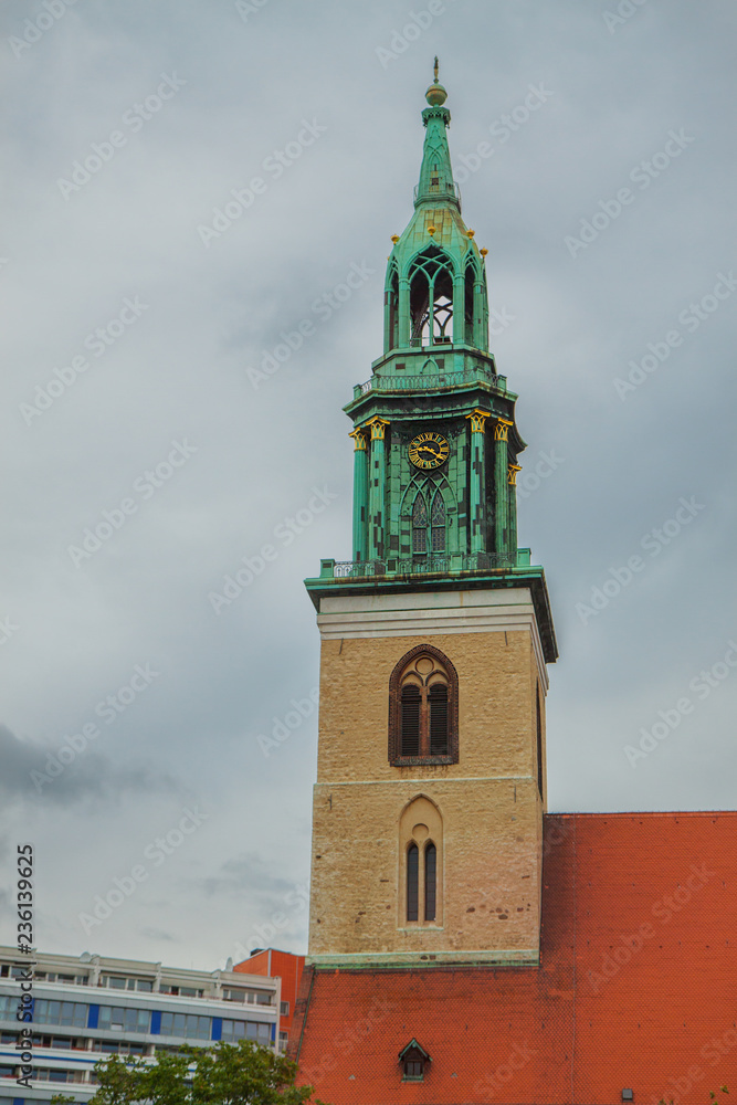   Beautiful tower with a spire and gold ornaments. Red brick roof religious buildings. Old architecture, clock tower. Cityscape.