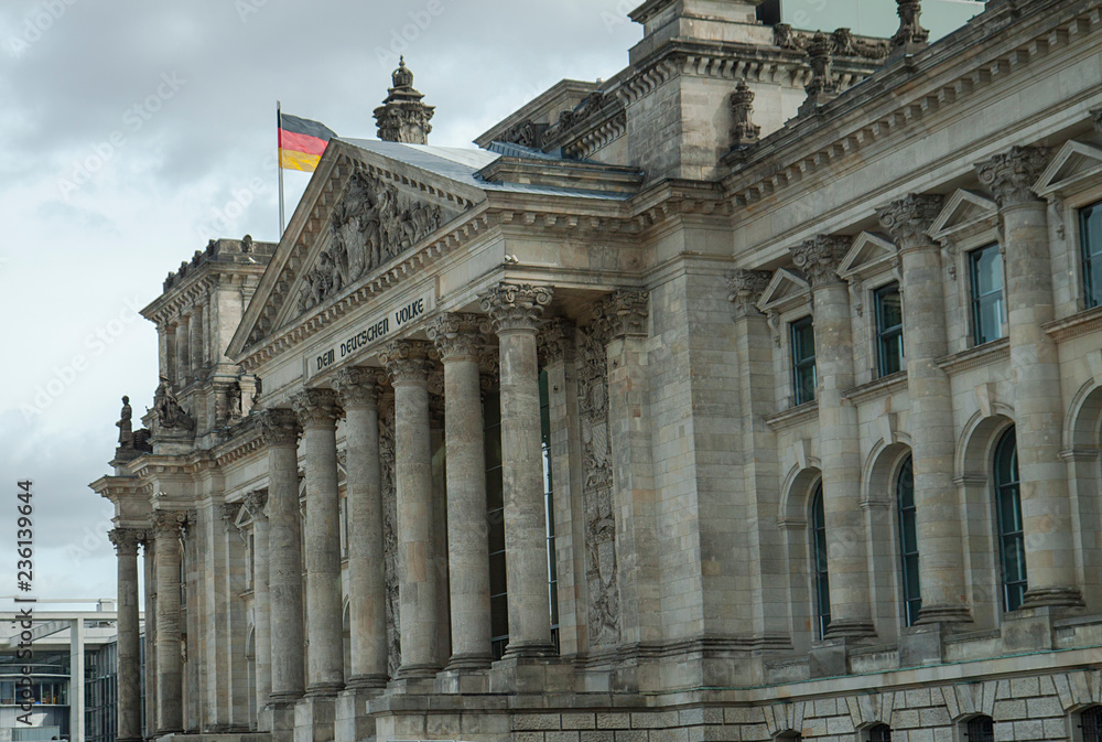 The majestic old building of the Reichstag Parliament in Berlin. Gray building on a cloudy sky background. German flags.City landscape.