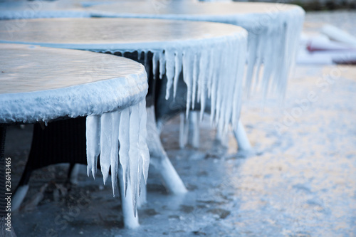 Icicles on tables in cafe outside. Abnormal cold weather. Winter sea. Ice and frozen floor.