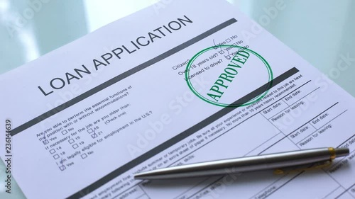 Loan application document approved, hand stamping seal on official paper closeup