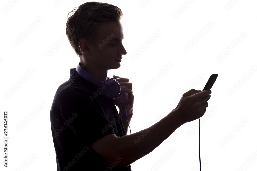 silhouette of a young man with headphones on his neck,a guy flips through a playlist of music on his player on white isolated background silhouette of a young man with headphones on his neck,a guy flips through a playlist of music on his player on white isolated background