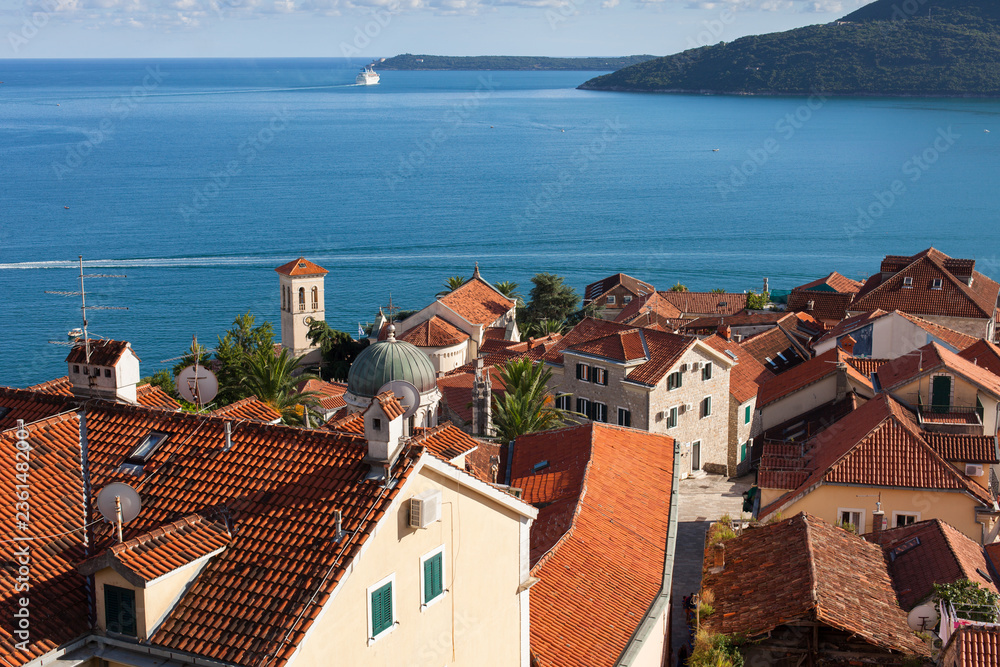Fototapeta premium Montenegro, Herceg Novi. Tiled roofs of old town at background of the Adriatic Sea, mountains, cruise liner. Ancient mediterranean architecture.