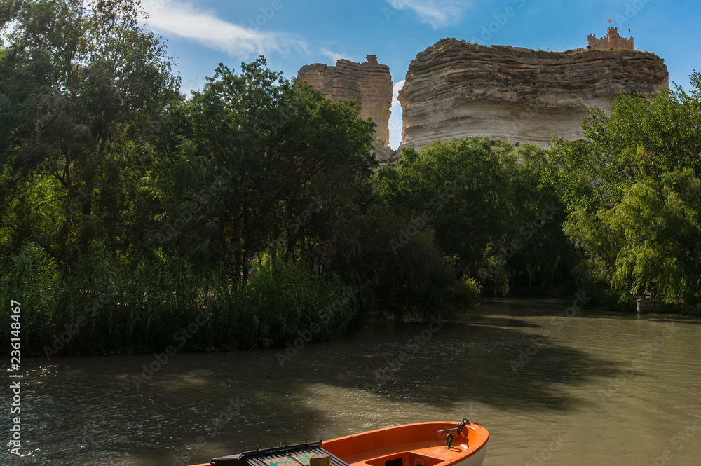 Boat on the river and castle at the top of the rocks in Alcalá del Júcar