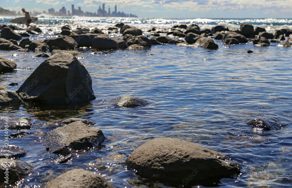 Calm Rockpool with surfer out of water with surfboard and city in the distance Calm Rockpool with surfer out of water with surfboard and city in the distance