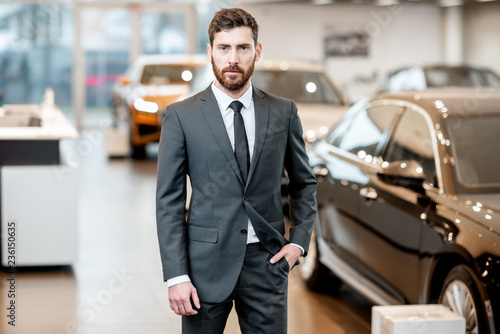 Wallpaper Mural Portrait of a handsome salesman in the suit standing at the showroom with luxury cars on the background Torontodigital.ca