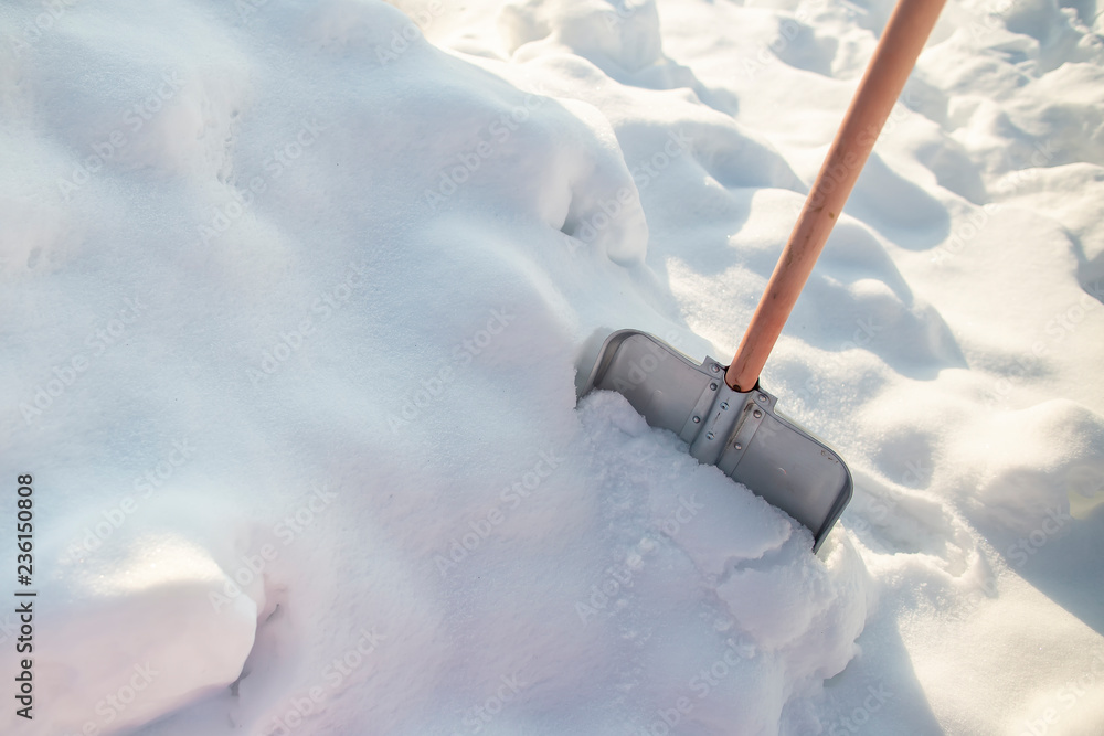 Metal shovel with a wooden handle, standing in a snowdrift, on a background of white snow, on a sunny frosty day. Metal shovel with a wooden handle, standing in a snowdrift, on a background of white snow, on a sunny frosty day.