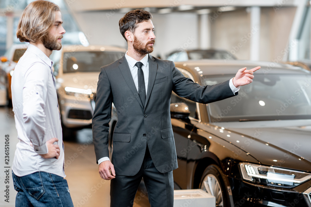 Professional car salesman talking with male client showing new cars at the showroom