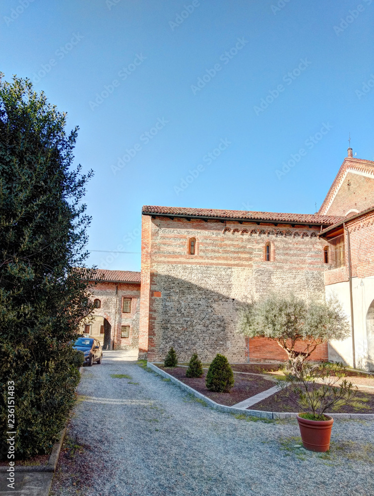 The cotto brick, round arches side arcade and bell tower of the rural Saints Nazarius and Celsus abbey in San Nazzaro Sesia, Piedmont region, Italy