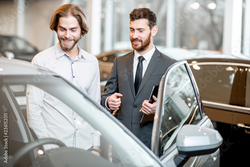 Car salesman helping a young male client to make a decision showing intrerior of a luxury car at the showroom © rh2010