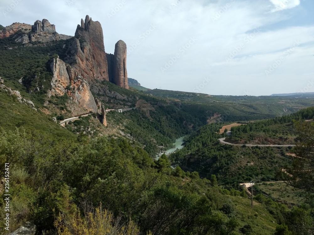 A landscape of Mallos de Riglos mountains, with high canyon like peaks, next to the Gallego river, during a sunny summer day, in Aragon region, Spain