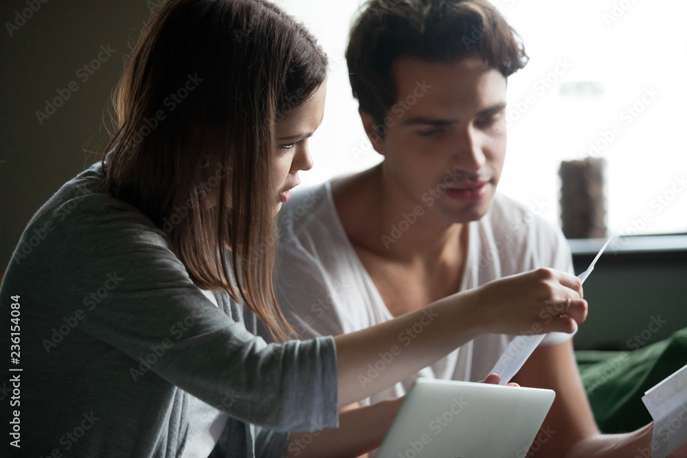 Fototapeta premium Close up stressed millennial couple sitting on sofa at home and check unpaid bills, taxes, due debt and bank account balance. Bankruptcy, debt and lack of money, financial problems in family concept