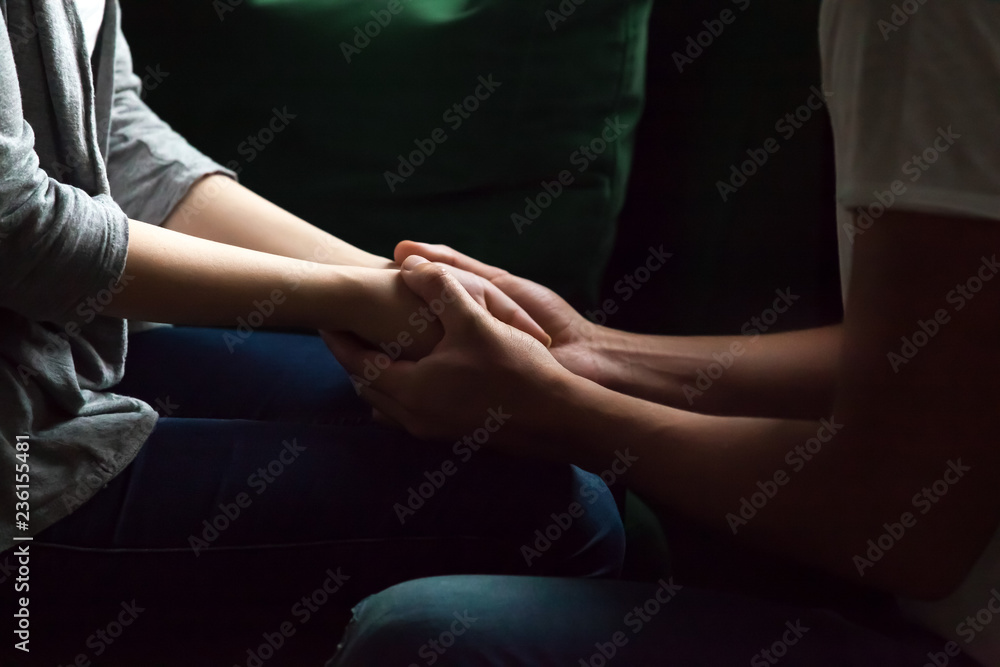 Close up woman and man in love sitting on couch, two people holding hands. Symbol sign of sincere feelings, compassion, loved one, say sorry. Reliable person, trusted friend, true friendship concept