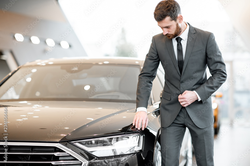 Portrait of an elegant businessman touching headlight of a luxury car in the showroom
