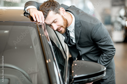 Businessman touching with face a new luxury car in the showroom