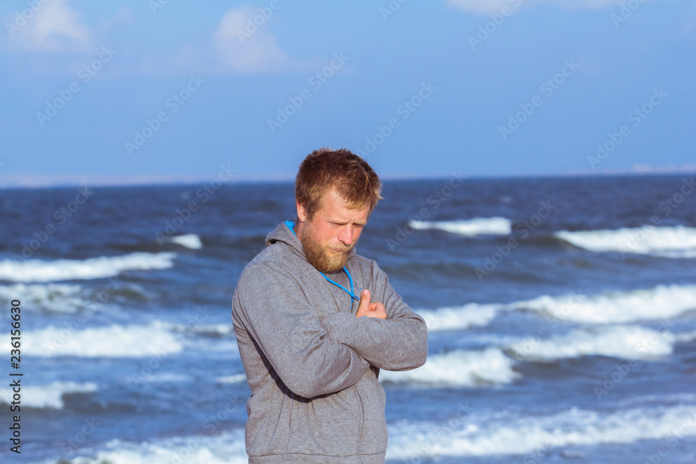 portrait of young blonde bearded man in gray hoody walking on the beach in dreamy mood portrait of young blonde bearded man in gray hoody walking on the beach in dreamy mood