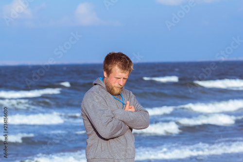 portrait of young blonde bearded man in gray hoody walking on the beach in dreamy mood