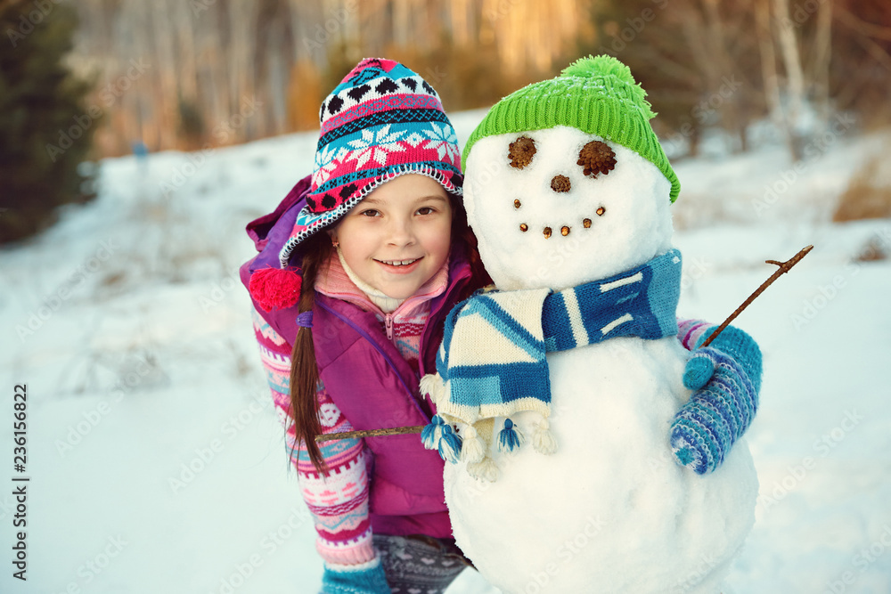 happy kid playing with snowman in the winter outdoors