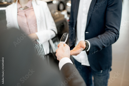Salesperson giving keys from a new car to a business couple in the car showroom  close-up view with no face