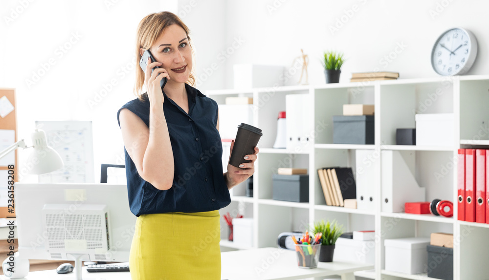 A young girl talking on the phone in the office and holding a glass of coffee. A young girl talking on the phone in the office and holding a glass of coffee.